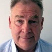Middle-aged man with grey hair wearing a light blue collared shirt, facing the camera, neutral background.
