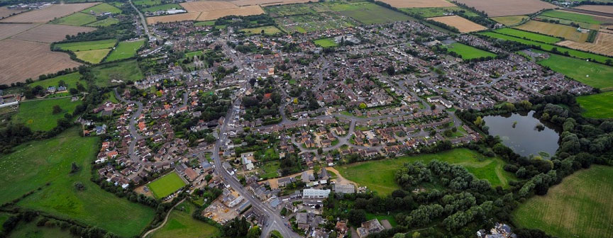 Aerial view of a small town surrounded by fields, trees, and a pond on the outskirts.