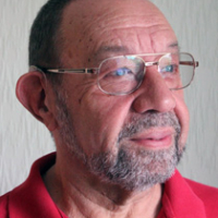 Older man with glasses, short hair, and a beard, wearing a red collared shirt, looking to the side.