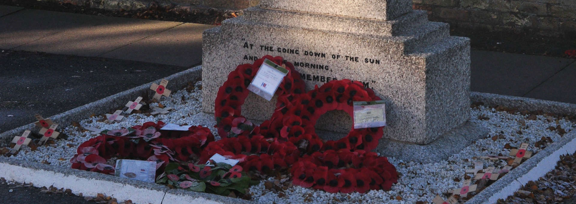 Poppy wreaths and remembrance crosses placed at the base of a stone war memorial.
